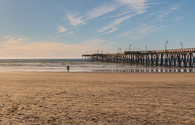 Pier on beach against sky during sunset