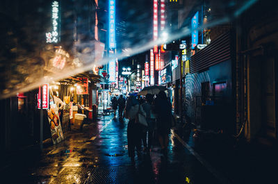 Rear view of people walking on wet street at night