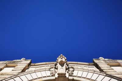Low angle view of statue against building against blue sky