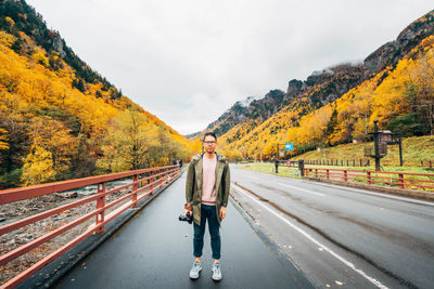 Portrait of man standing on sidewalk against sky during autumn