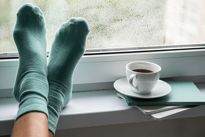 Coffee cup, books and woman legs against wet window. rest and reading at rainy day.