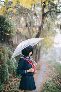 Woman with umbrella standing against trees during rainy season