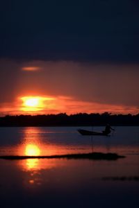 Silhouette man on boat against orange sky