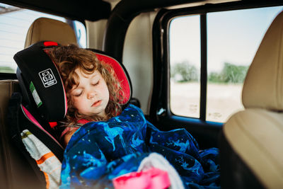 Young girl asleep in carseat on long drive on sunny day
