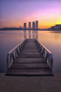 Sea by buildings against sky during sunset