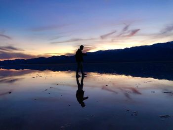 Silhouette man standing on shore against sky during sunset