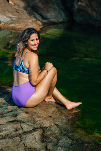 Portrait of woman sitting on rock by sea