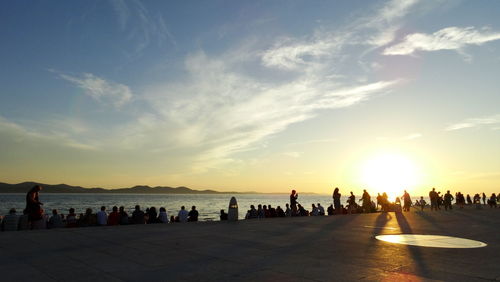 Silhouette people on beach against sky during sunset