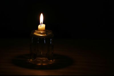 Close-up of illuminated tea light candle on table in darkroom