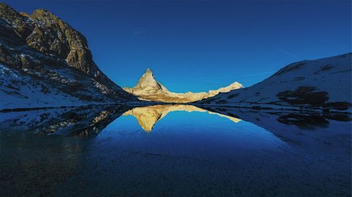 Scenic view of lake and mountains against clear blue sky