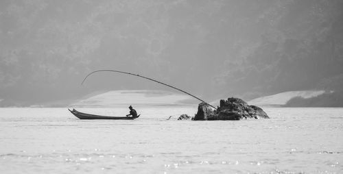 Silhouette man fishing in sea against sky