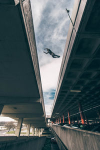 Low angle view of man jumping over bridge in city