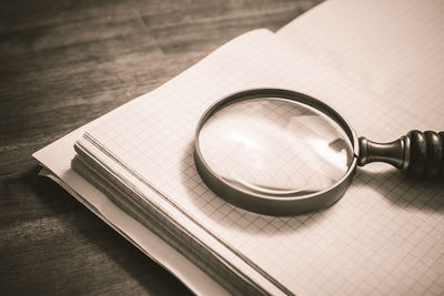 High angle view of magnifying glass with book on wooden table