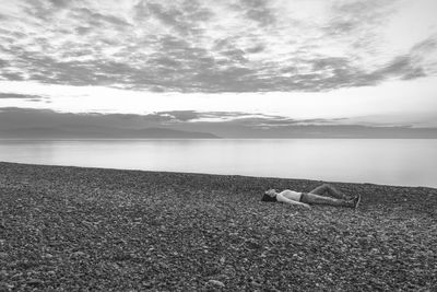 Full length of woman lying on pebble beach against sky