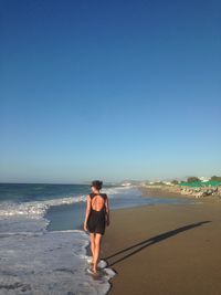 Rear view of man walking on beach against clear sky