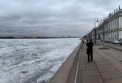 Man standing on sea by city against sky