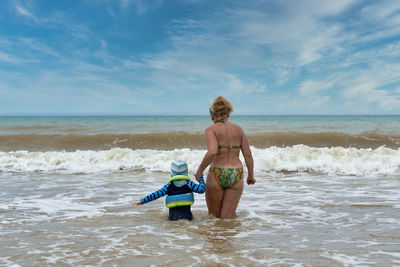 Rear view of shirtless boy on beach against sky