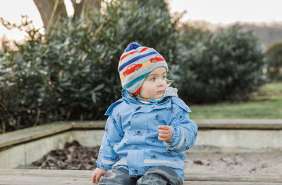 Cute girl wearing warm clothing looking away while sitting outdoors