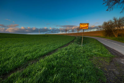 Road sign on field against blue sky