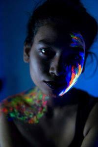 Close-up portrait of young woman with paint on face and body in darkroom