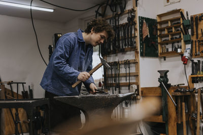 Blacksmith using hammer and anvil in workshop