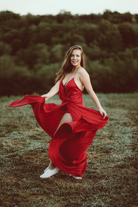 Portrait of smiling young woman wearing red dress standing on land