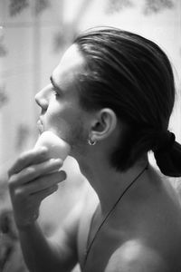 Shirtless young man applying soap on face in bathroom at home