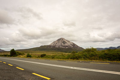 Empty road leading towards mountain against sky