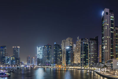 Illuminated buildings by river against sky in city at night