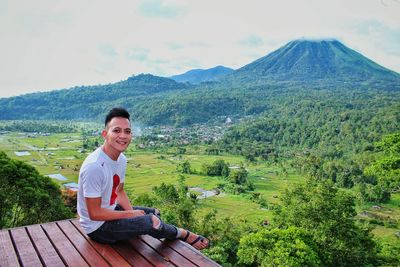 Portrait of man sitting on observation point against sky