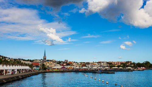 View of buildings by river against cloudy sky