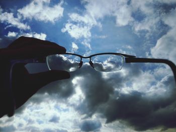 Low angle view of hand holding sunglasses against sky