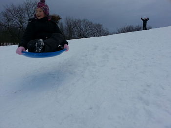 Full length of girl sitting on snow covered landscape during winter