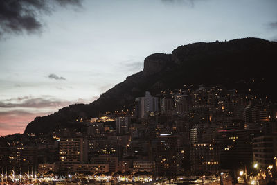 Illuminated buildings in city by mountain at dusk