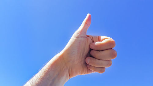 Low angle view of hand against blue sky