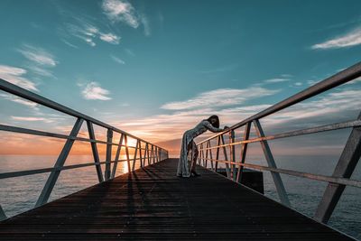 Man standing on pier by sea against sky during sunset