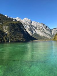 Scenic view of lake by mountains against clear blue sky