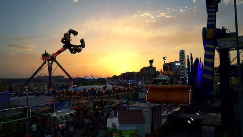 People in amusement park against sky during sunset