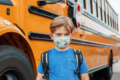 Boy kid student in protective face mask near school yellow bus outdoors. new normal at coronavirus 