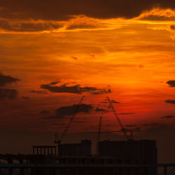 Silhouette of factory against orange sky