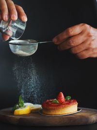 Cropped image of hand sprinkling sugar on strawberry tart