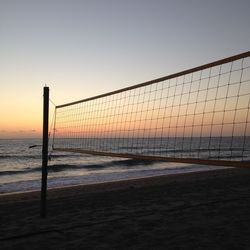 Volleyball net on beach against sea during sunset