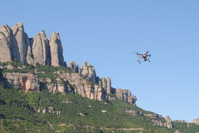 Low angle view of octocopter flying by rocks against clear sky