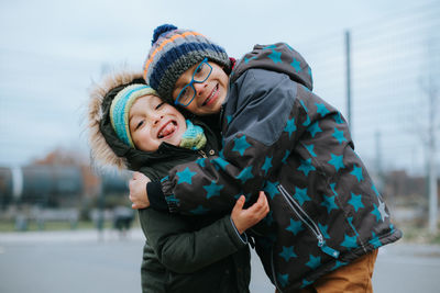 Cute boys embracing while standing outdoors during winter