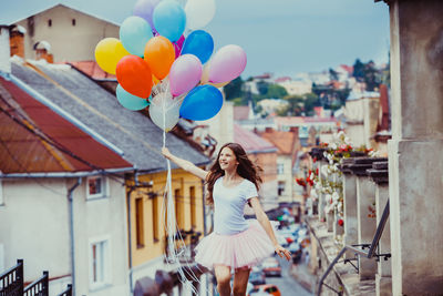 Full length of woman with balloons standing against buildings in city