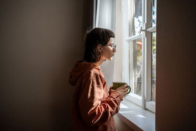 Side view of woman looking through window