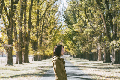 Young woman standing on road against trees in park during sunny day