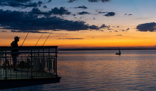 Silhouette fisherman on sea against sky during sunset
