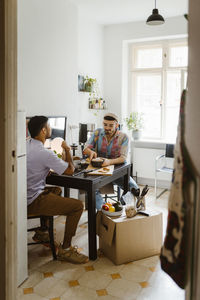 Boyfriends having food while sitting on dining table seen through doorway