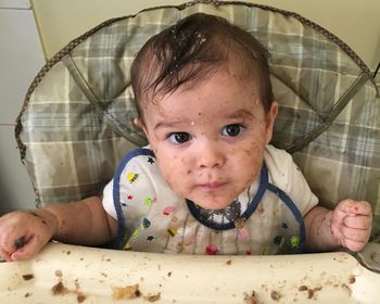 Close-up portrait of messy baby boy sitting on high chair